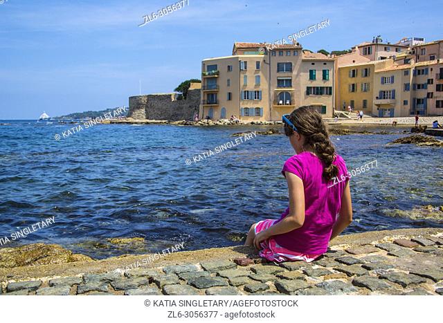 A preteen all dress in pink playing on the side of the bay of Saint Tropez. We can see the city village of Saint Tropez in France behind her