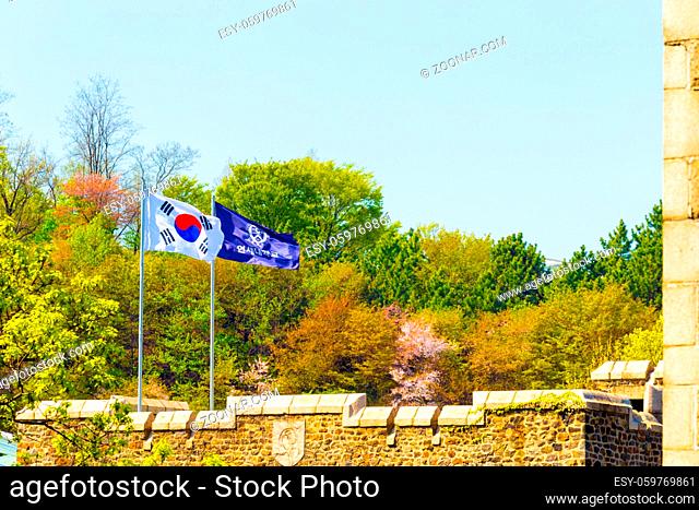 The flag of Yonsei University and national Korean Taegukgi flag flying above a main quad building in front of blossoming spring trees on the main Sinchong...