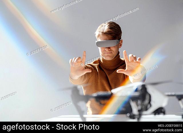 Businessman wearing virtual reality simulator making finger frame towards drone in office