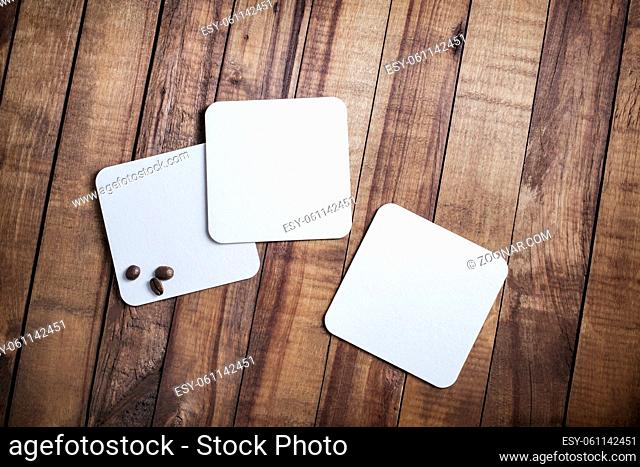Photo of three blank white square beer coasters and coffee beans on wood table background. Top view. Flat lay