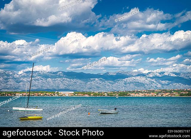 Motorboats and sailboats anchored near Zdrijac beach between Nin bay and Adriatic Sea with mountain range of Dinaric Alps in the background