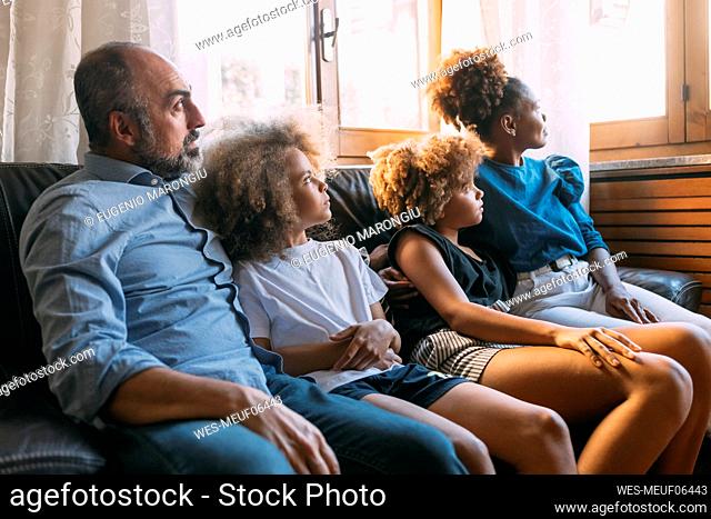 Man with family looking through window sitting on sofa at home