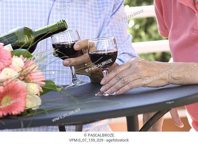 Mid section view of a senior man pouring red wine into wine glasses
