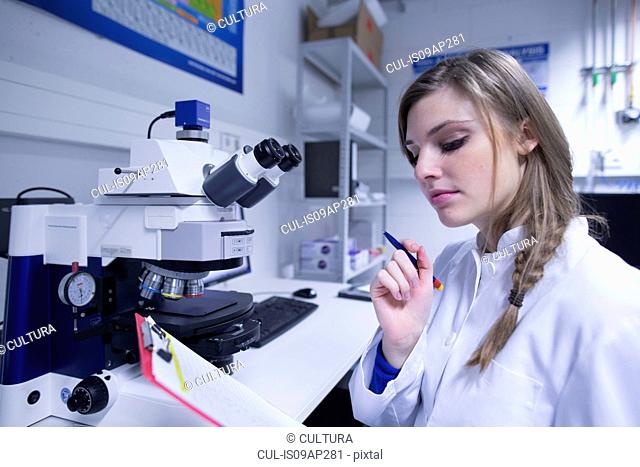 Female scientist reading notes on clipboard in lab