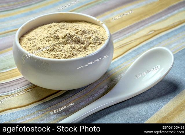 ashwagandha root (aka Indian ginseng) powder in a small ceramic bowl with a teaspoon, superfood concept