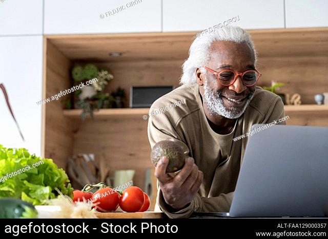 Senior man watching recipe on laptop while leaning on kitchen worktop