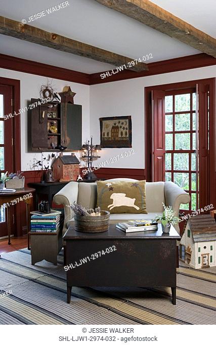 SITTING AREAS: Sette sofa, with rabbit pillow, cranberry red painted trim, folk art accents, stacks of books, trunk as coffee table