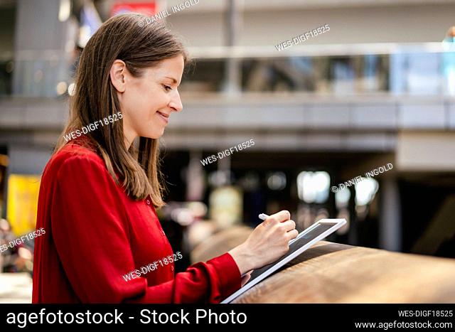 Smiling businesswoman using digitized pen on tablet PC at workplace