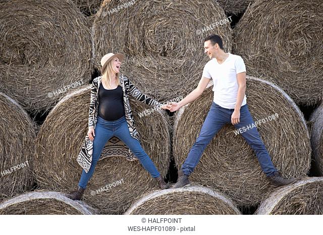 Happy expectant parents standing on bales of straw