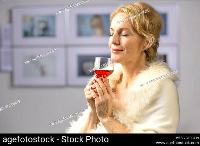 Smiling woman with wineglass standing at opening ceremony of exhibition