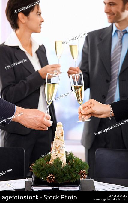 Business people raising toast over meeting table with Christmas decoration at office. Focus placed on flutes in front
