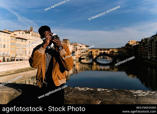 Young man taking a picture on a bridge above river Arno, Florence, Italy