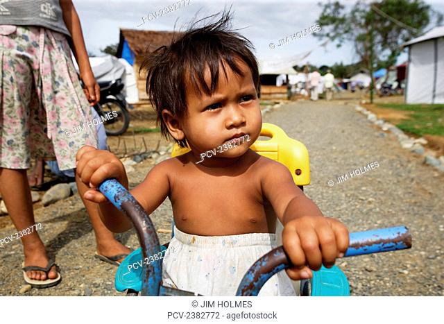 Young child on tricycle in a camp for displaced people near Meulaboh after the Indian Ocean tsunami in December 2004; Lhok Nga, Aceh Province, Sumatra