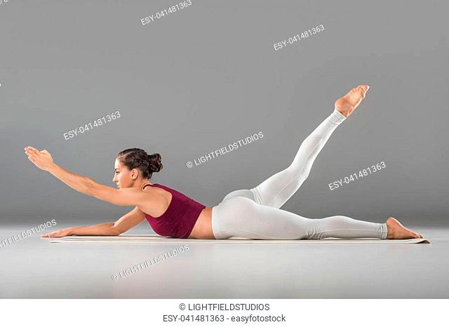 side view of beautiful sporty young woman doing yoga exercise on grey