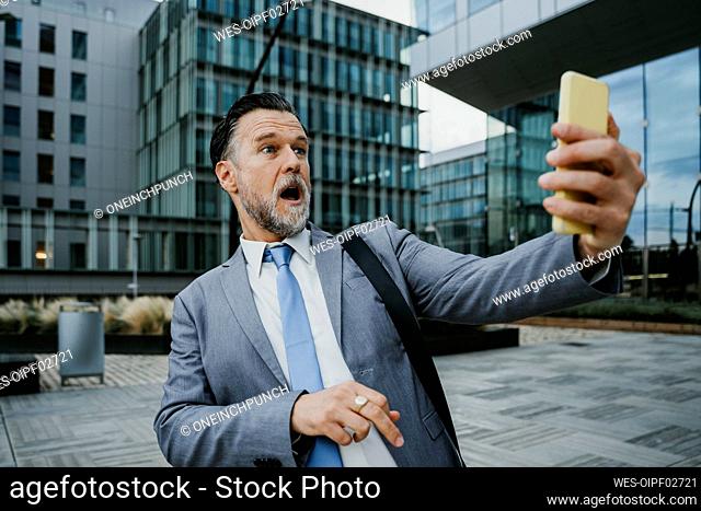 Shocked businessman watching mobile phone on footpath