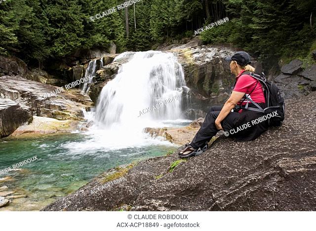 Woman hiker sitting on rock looking at waterfalls in Golden Ears Provincial Park in Maple Ridge, British Columbia, Canada