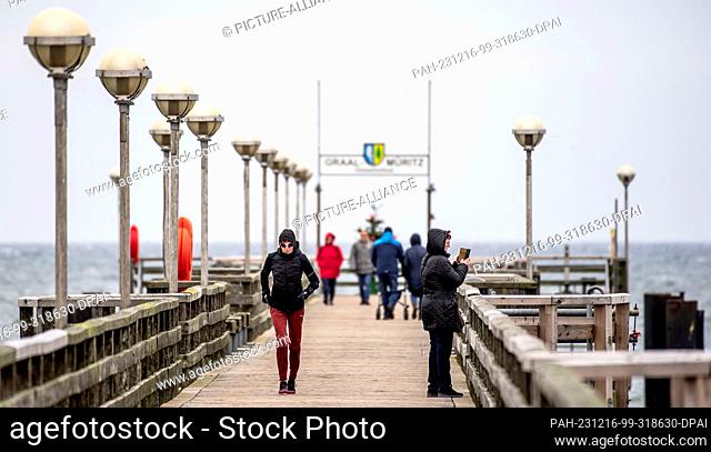 16 December 2023, Mecklenburg-Western Pomerania, Graal-Müritz: Strollers walk along the pier at the Baltic seaside resort