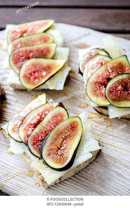 Bruschetta toasted sliced sourdough bread with cheese and figs drizzled with honey on a white wooden serving board on a wooden table