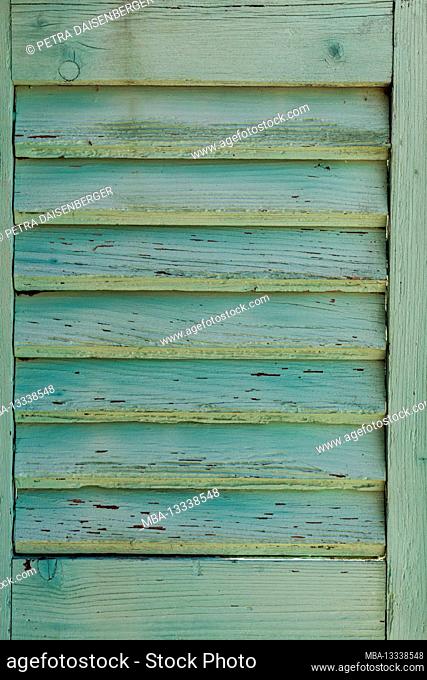 A wooden shutter with a turquoise blue paint that is peeling off
