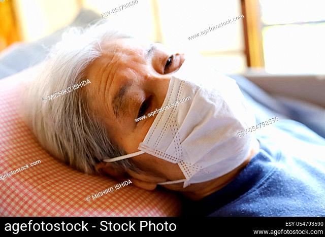 Senior lady lying on the nursing care bed with the surgical mask for virus protection