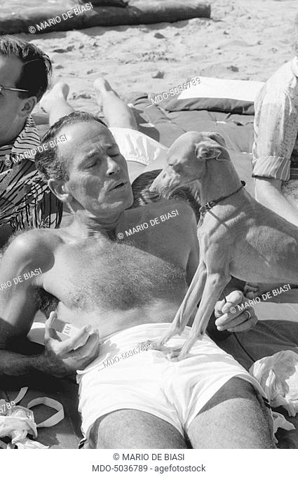 American actor Henry Fonda on the beach with a puppy dog during the XVIII Venice International Film Festival. Venice, 1957
