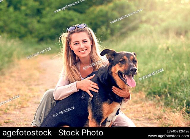 Happy smiling black dog wearing a walking harness sitting facing its pretty young woman owner who is caressing it with a loving smile outdoors in countryside