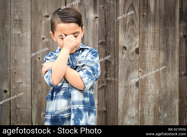 Young frustrated mixed-race boy with hand on face against wooden fence
