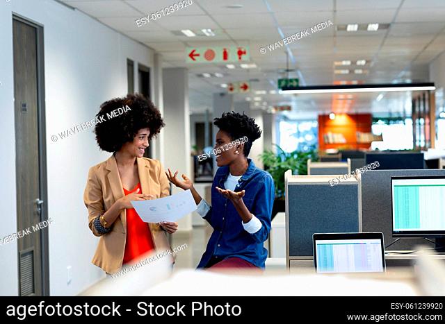 Happy biracial female colleagues discussing over document during meeting in modern workplace