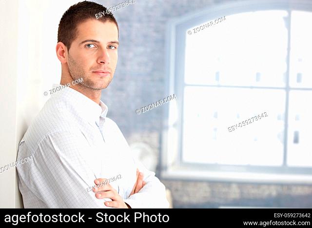 Handsome young man standing arms crossed by wall
