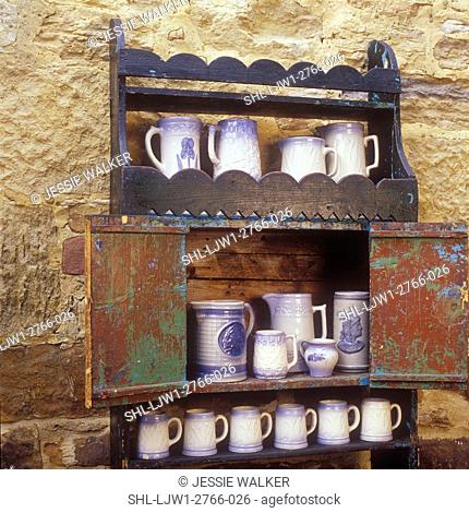 COLLECTIONS DISPLAYS - An antique open cupboard made by German immigrant in 1850. A collection of Salt Glaze Pottery on shelves, stone wall as background
