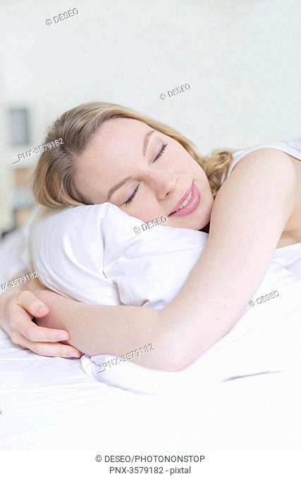 Pretty blonde woman smiling with eyes closed in bed