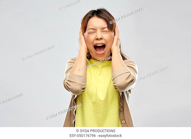 stressed asian woman closing ears and screaming
