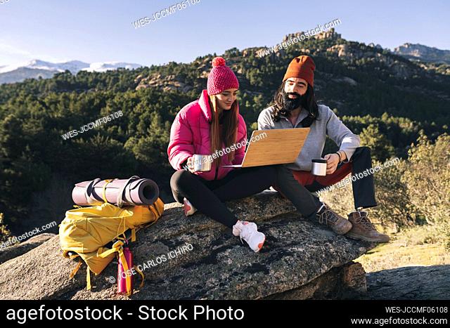Young woman sharing laptop with boyfriend sitting on rock