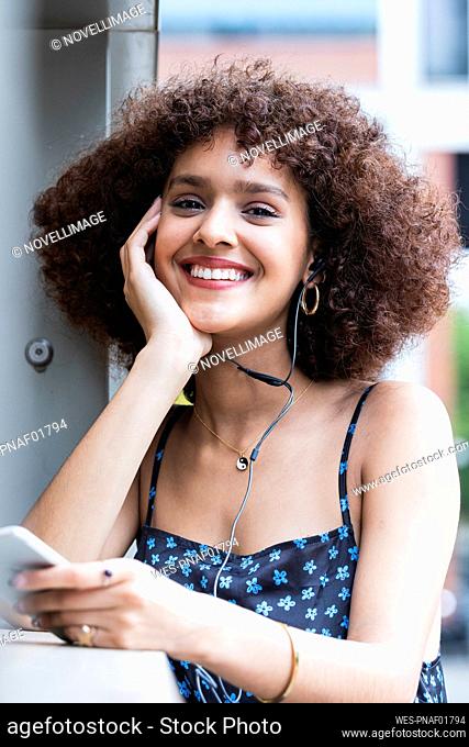 Young woman with hand on chin smiling while holding mobile phone