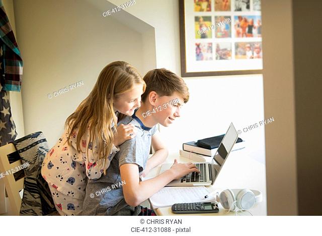 Sister watching brother using laptop in bedroom