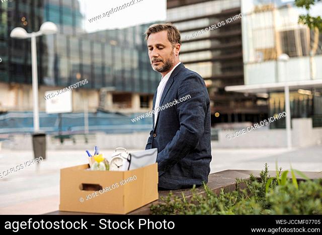 Businessman sitting with cardboard box outside office building