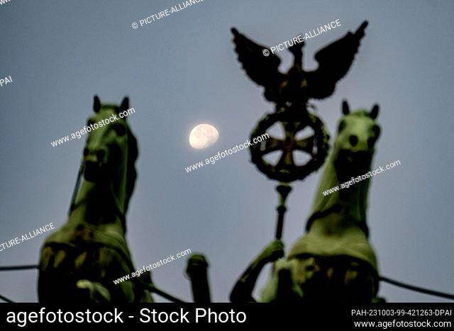 03 October 2023, Berlin: The moon sets behind the Brandenburg Gate in the early morning on the anniversary of the reunification of the two German states on...