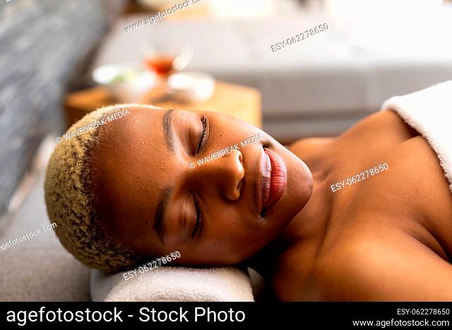 Happy african american woman lying on towel with eyes closed