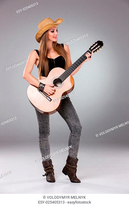 The beautiful girl in a cowboy's hat playing acoustic guitar on a gray background. Portrait in full growth