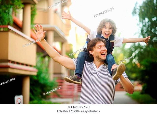 First grader sitting on the shoulders of his father. He is very happy. Father and son pretending to fly. They have a good mood