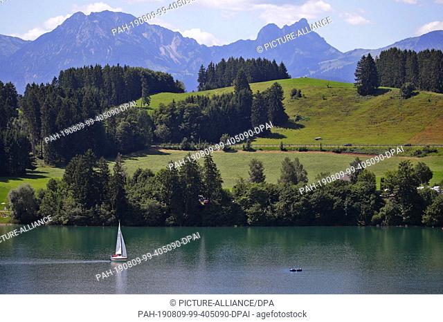 09 August 2019, Bavaria, Roßhaupten: A sailing boat sails over Lake Forggen in front of the panorama of the Alps. Photo: Karl-Josef Hildenbrand/dpa