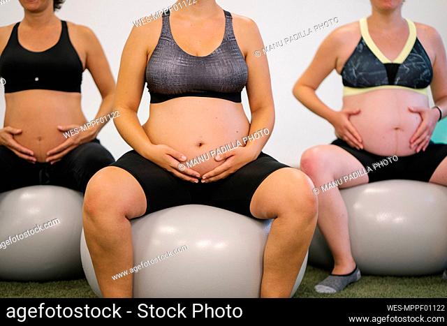 Midsection of pregnant woman sitting on fitness ball at yoga studio