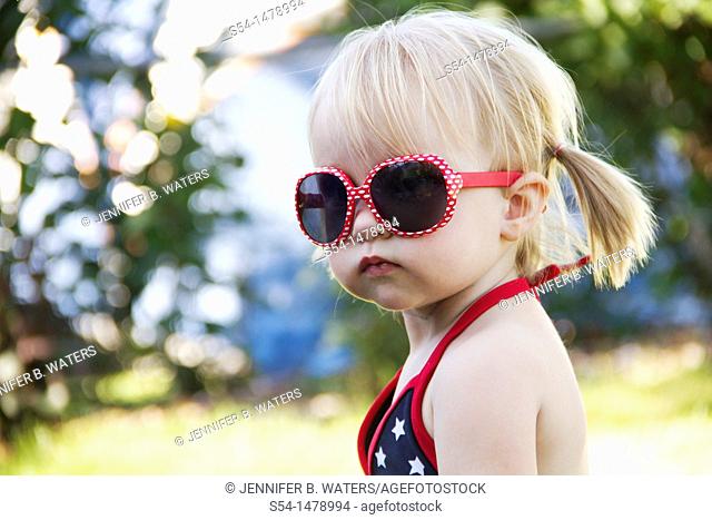 A one year old toddler wearing bright red sunglasses on Independence Day in Liberty Lake, Washington, USA
