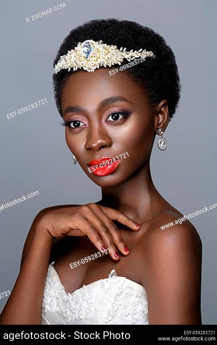 Beautiful black skin young woman with red lips in white gown and pearl tiara. Beauty shot on grey background. Copy space