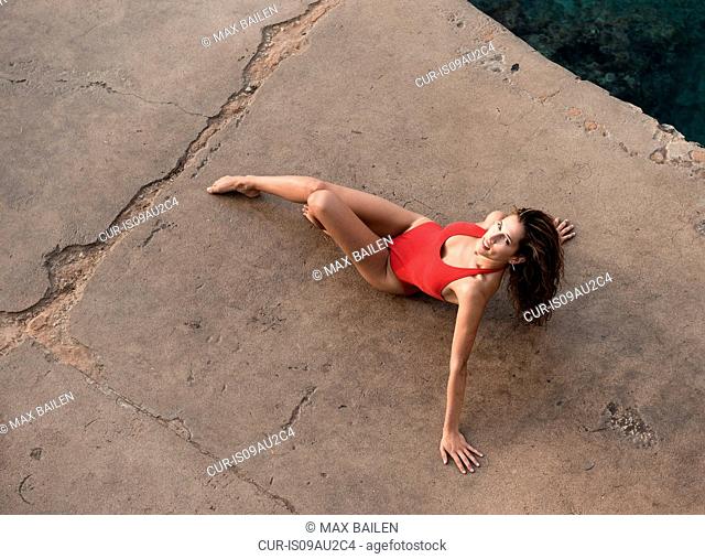 High angle portrait of young woman posing in red bathing costume on pier