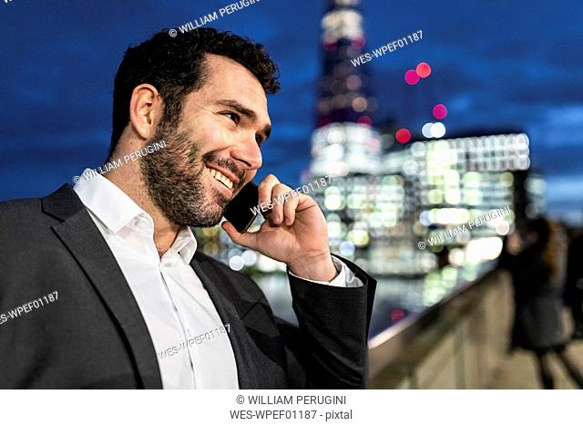 UK, London, portrait of smiling businessman talking on the phone while commuting by night