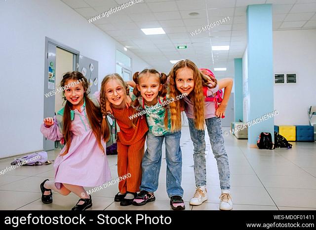 Joyful schoolgirls with arm around standing in school corridor