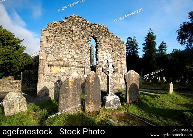 Tombstones and Celtic Cross memorial with the Round Tower seen through the lancet window of the ruins at Glendalough (or The valley of the Two Lakes)