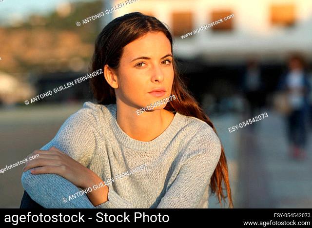 Serious teenage girl looking at camera defiant at sunset sitting in a town