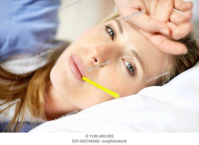Pretty young woman with thermometer , lying in bed with flu and fever